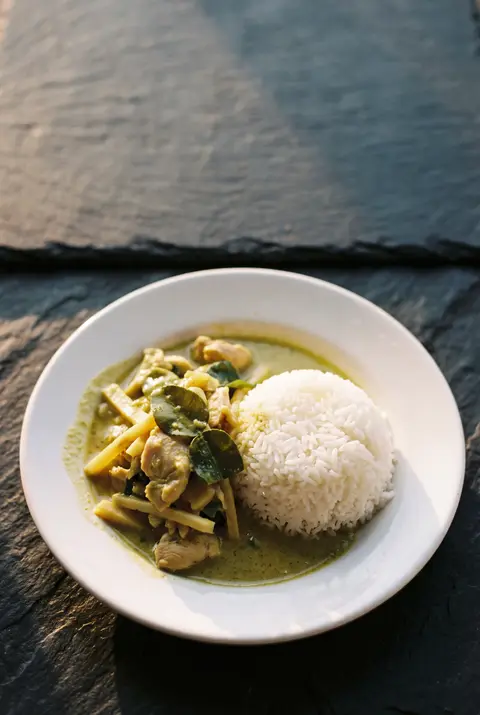 Thai green curry with chicken beside a portion of jasmine rice on a white plate