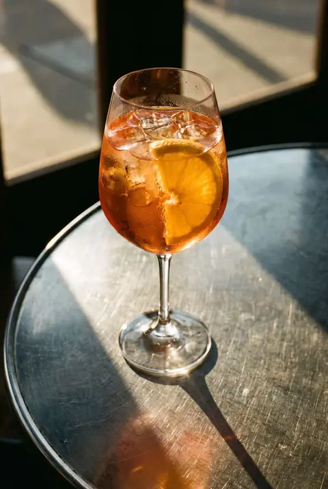 An Aperol spritz with ice and a slice of orange in a wine glass