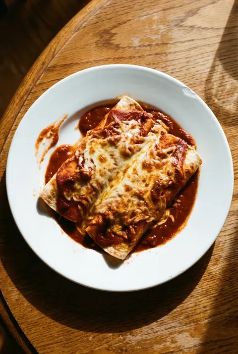 Two chicken enchiladas in red sauce with melted cheese on a white plate