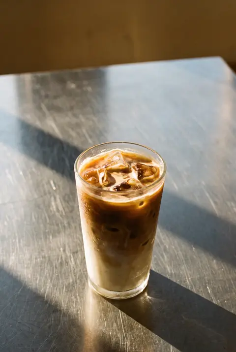 An iced latte with ice cubes and milk swirling into the coffee in a clear glass