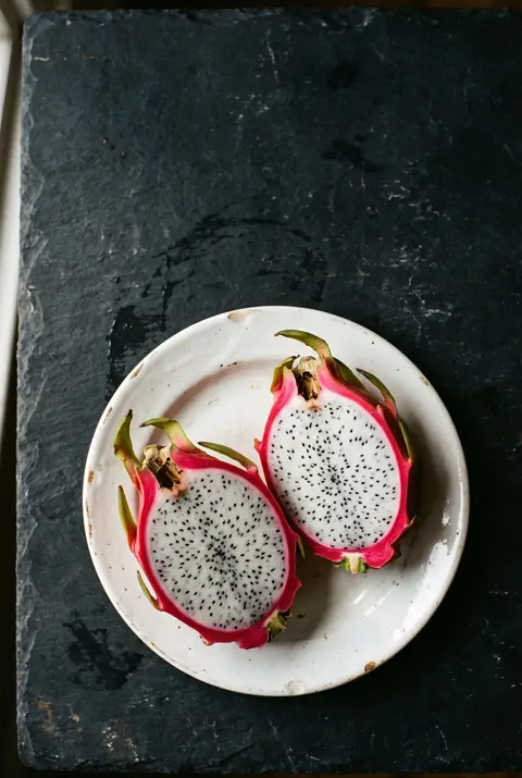 A dragon fruit cut in half showing white flesh with black seeds on a white plate