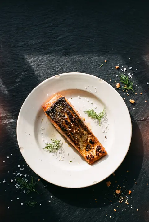 A cooked salmon fillet with crisp skin on a white plate