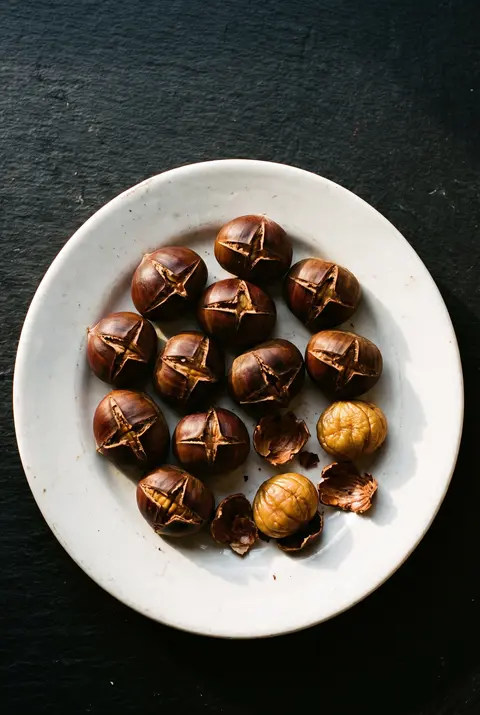Ten roasted chestnuts with split shells on a white plate
