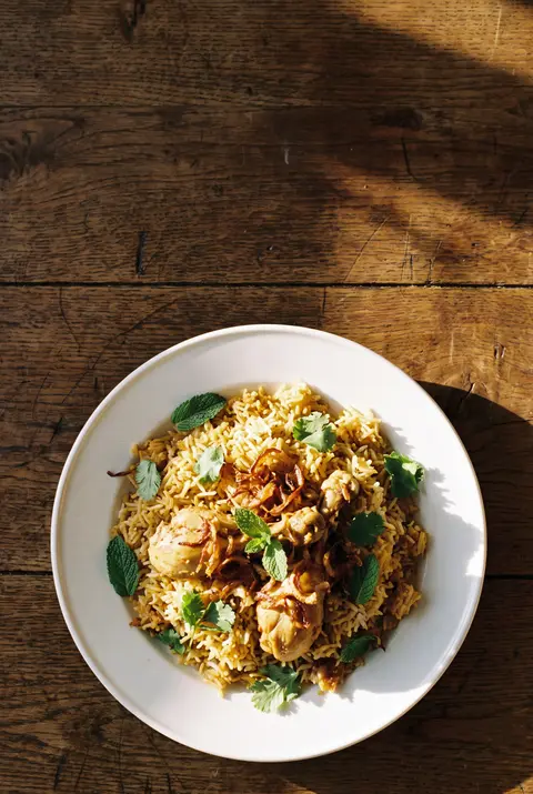 A plate of chicken biryani with fried onions and a few herbs on a white plate