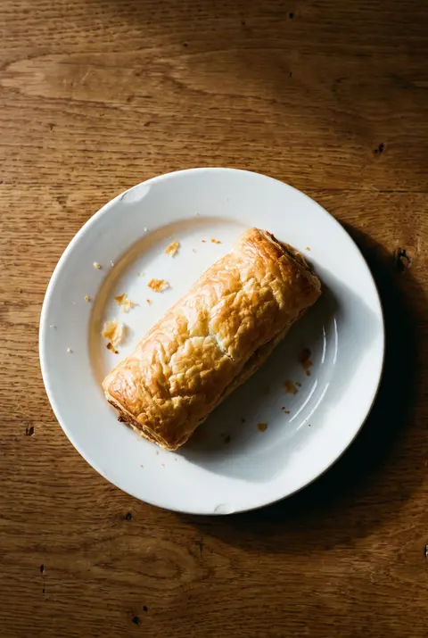 A golden bakery sausage roll with flaky pastry on a white plate