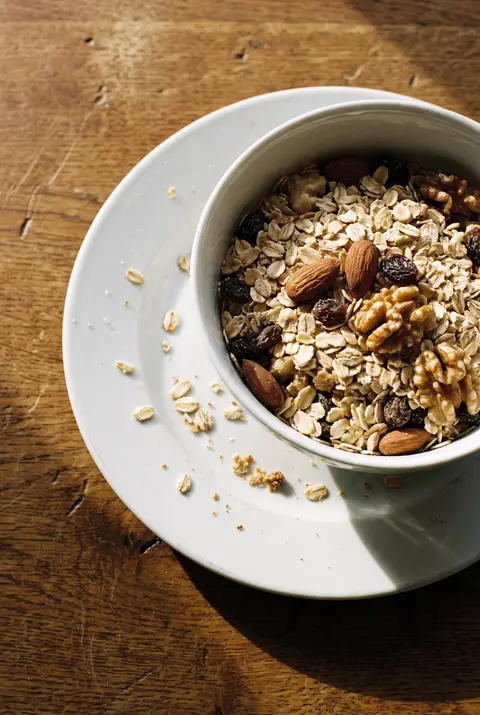 A white porcelain bowl of dry muesli with oats on a white plate