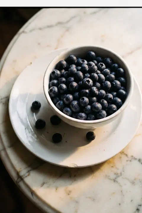 A white porcelain bowl of fresh blueberries on a white plate