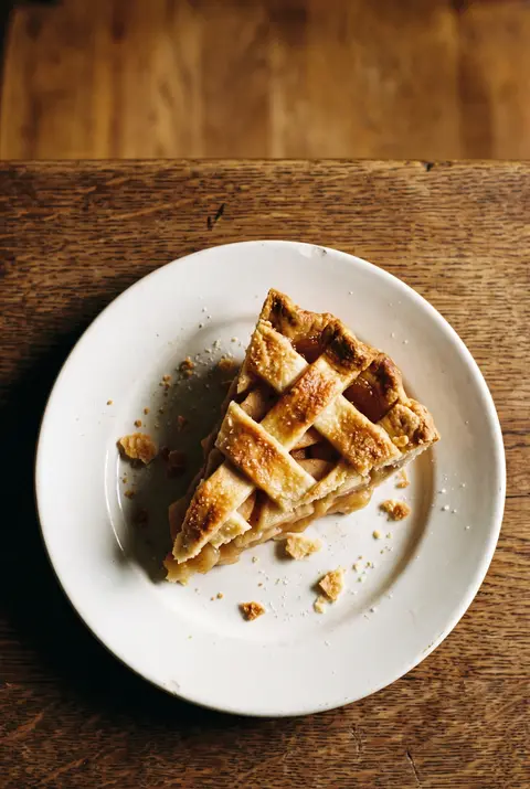 A slice of apple pie with a golden lattice crust and soft apple filling on a white plate