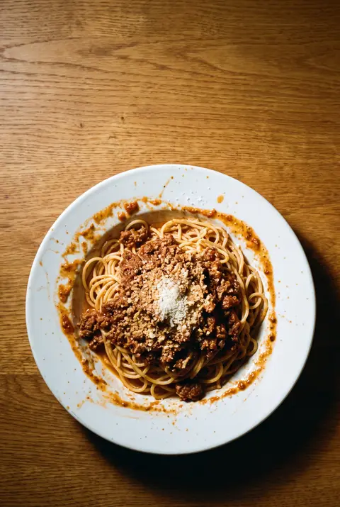 A plate of spaghetti with bolognese meat sauce and grated cheese on a white plate
