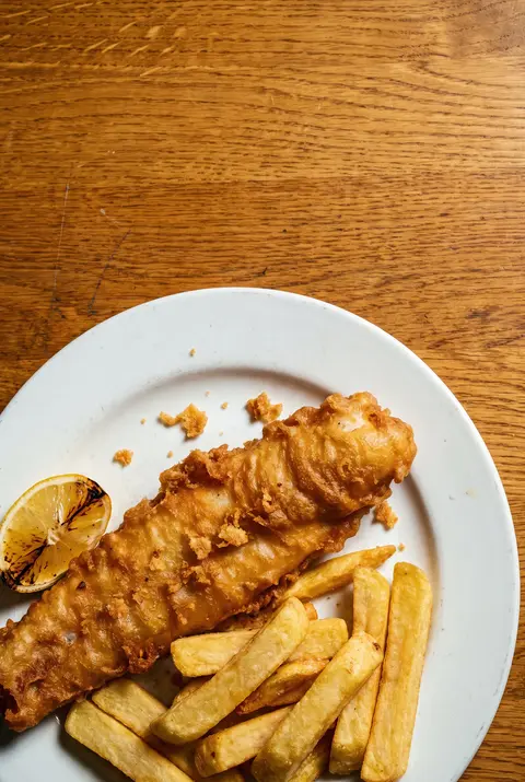 A battered fish fillet with a portion of thick chips and a wedge of lemon on a white plate
