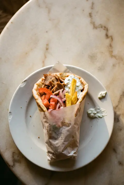 A pork gyros pita wrap with tomato on a white plate