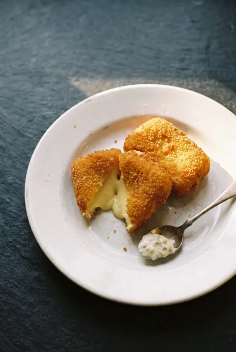 A portion of breaded fried cheese with a golden crust on a white plate