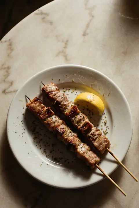 Two pork souvlaki skewers with a wedge of lemon on a white plate