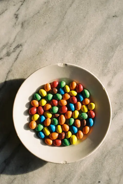 A small heap of colourful candy coated chocolate peanuts on a white plate
