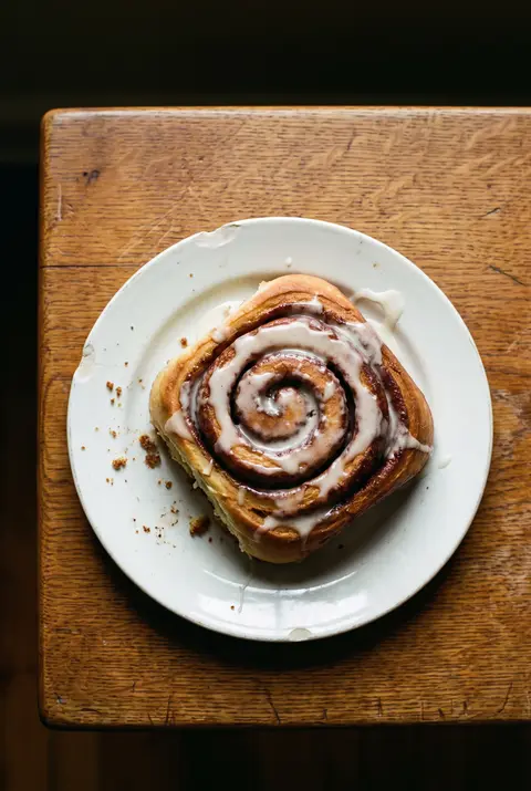 A large cinnamon roll with white icing melting into the swirls on a white plate
