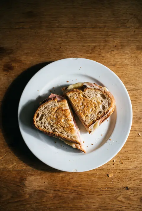 A ham and cheese sandwich on two slices of bread on a white plate