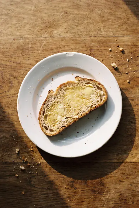 A slice of bread spread with a thin layer of butter on a white plate