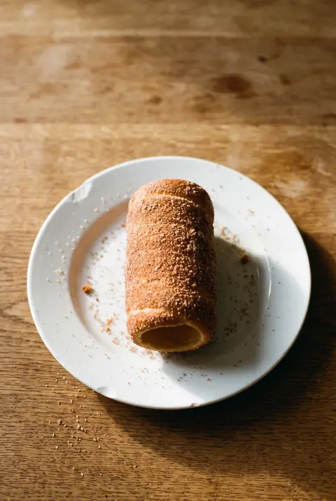A whole golden chimney cake rolled in cinnamon sugar on a white plate