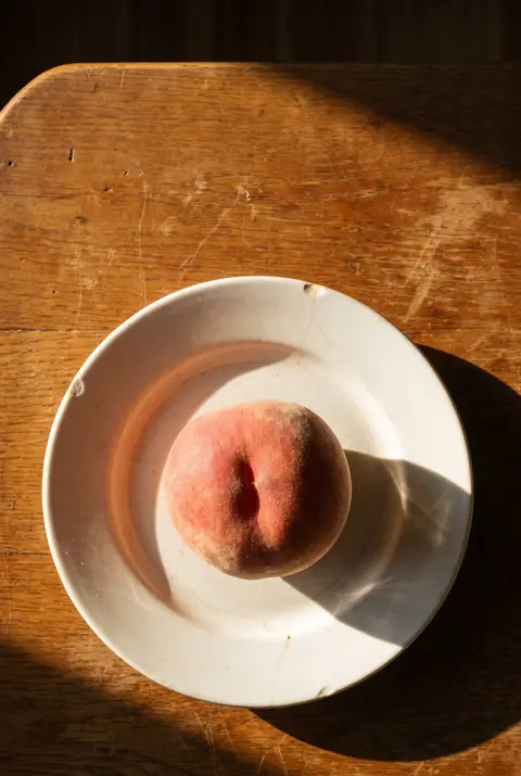 A ripe medium peach with a blush of red on a white plate