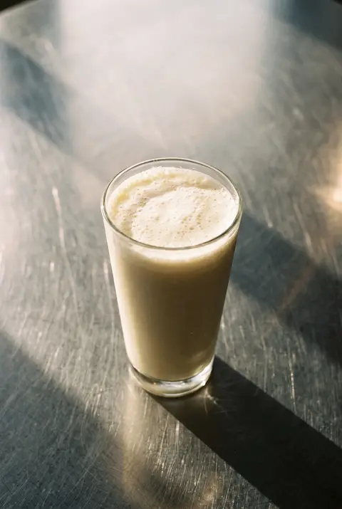 A vanilla protein shake with a light foam on top in a clear glass
