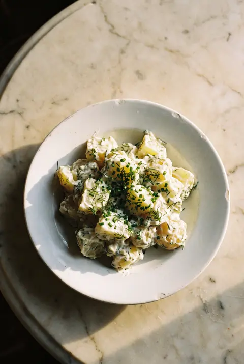 A portion of creamy potato salad with chives on a white plate