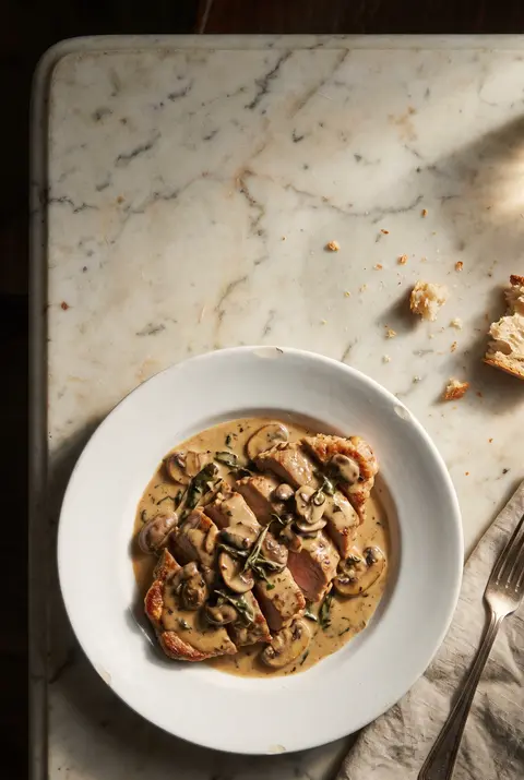 A plate of sliced veal in cream and mushroom sauce on a white plate