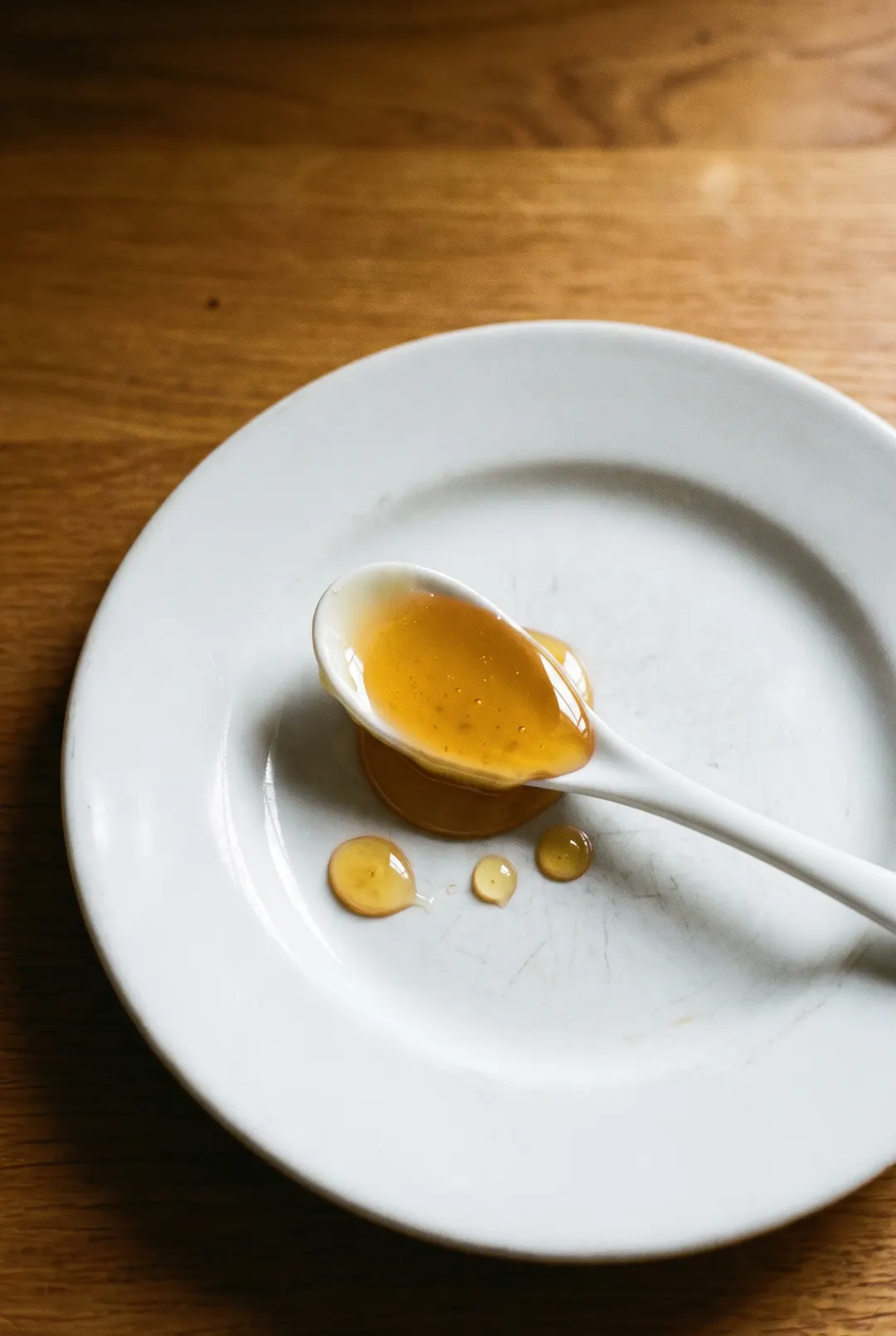 A tablespoon of golden honey in a small white porcelain spoon on a white plate