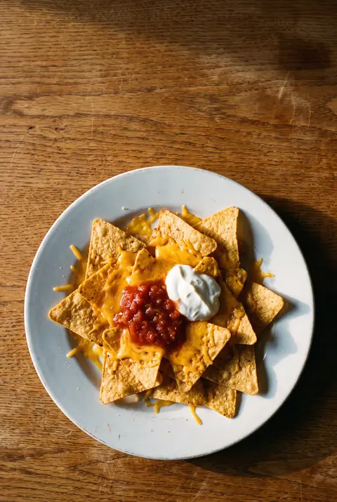 A plate of tortilla chips with melted cheese on a white plate