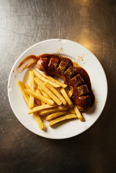 A sliced currywurst in curry ketchup dusted with curry powder on a white plate