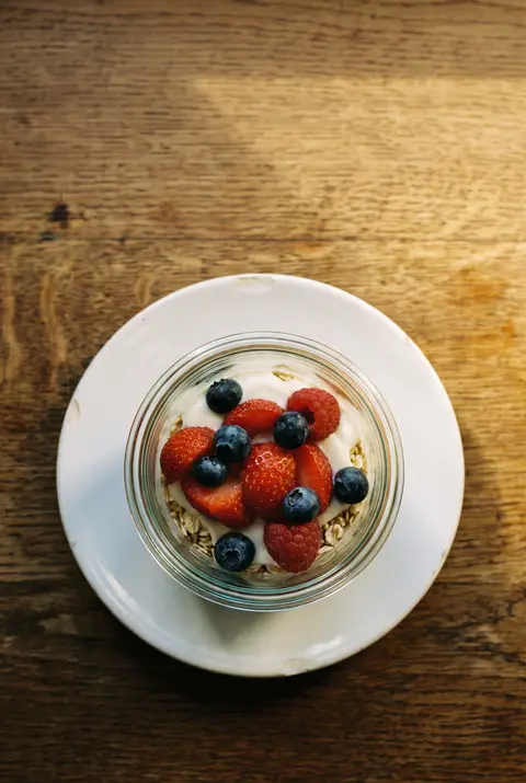 A glass jar of overnight oats layered with yoghurt and fresh berries on a white plate
