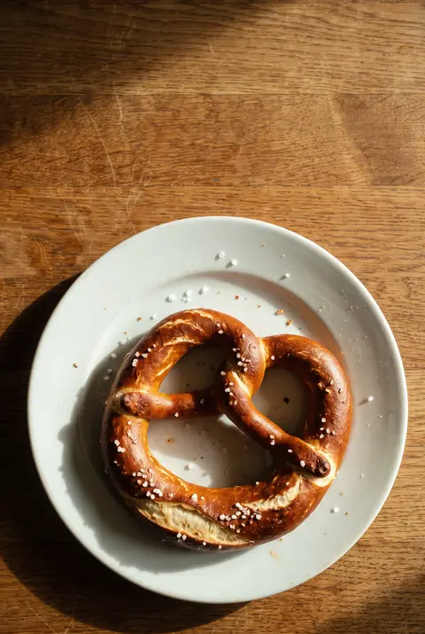 A large soft German pretzel with coarse salt and a deep brown crust on a white plate