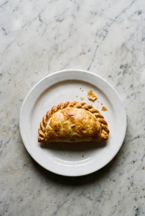 A golden baked beef empanada with a crimped edge on a white plate