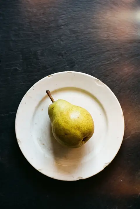 A ripe green yellow pear with a short stem on a white plate