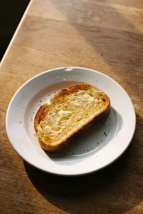 A slice of golden toast spread with butter on a white plate