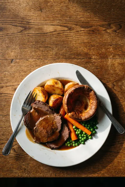 A full plate of roast beef with roast potatoes on a white plate