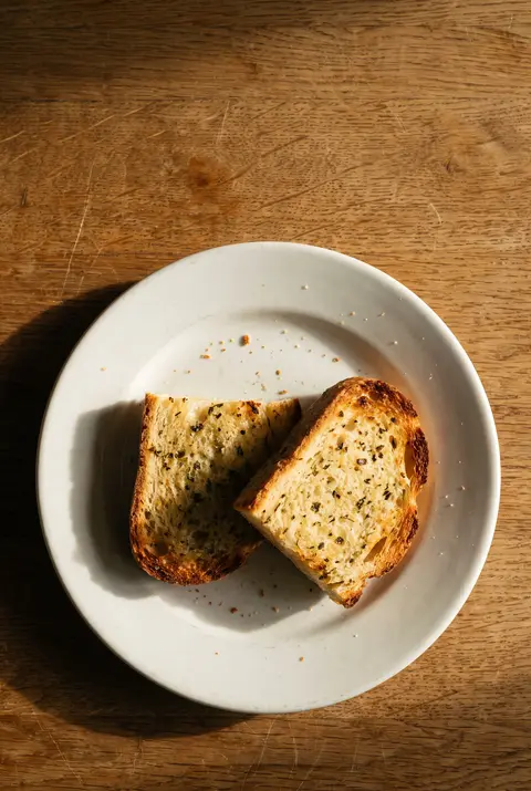 Two slices of garlic bread with herbs and golden edges on a white plate
