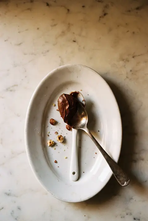 A tablespoon of chocolate hazelnut spread on a small white porcelain spoon on a white plate
