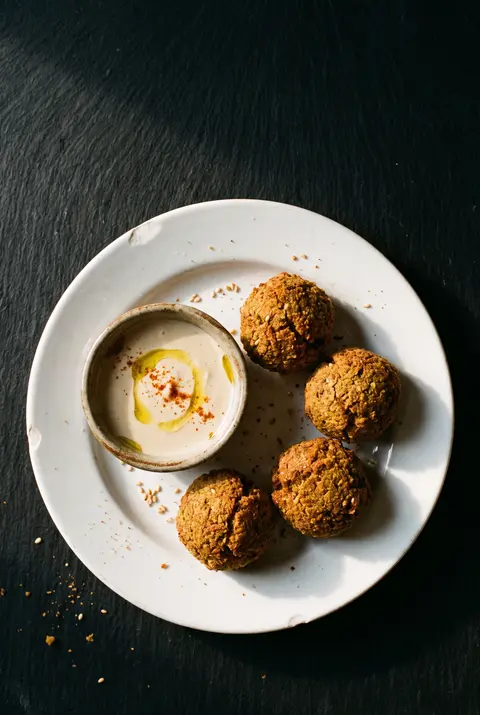 Four falafel balls with a small dish of tahini sauce on a white plate
