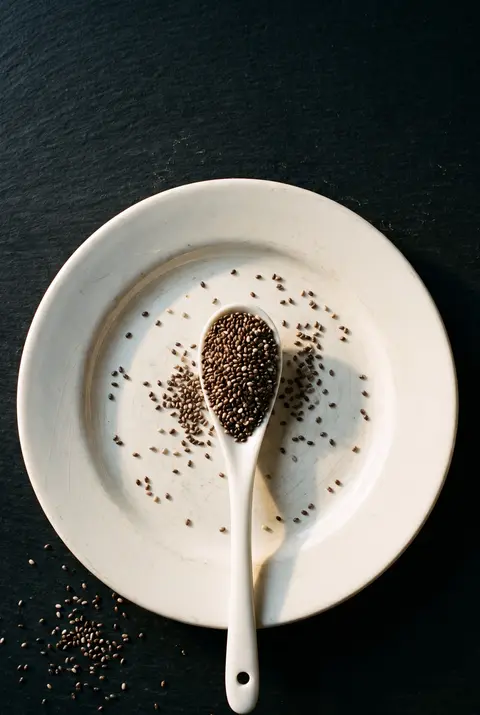 A tablespoon of chia seeds on a small white porcelain spoon on a white plate