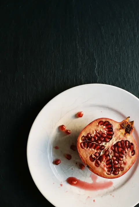 Half a pomegranate with its seeds showing on a white plate