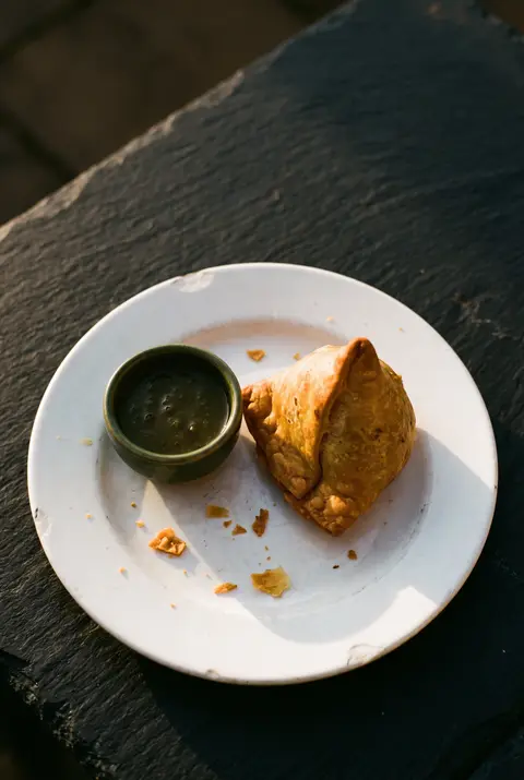 A golden vegetable samosa with a small dish of chutney on a white plate