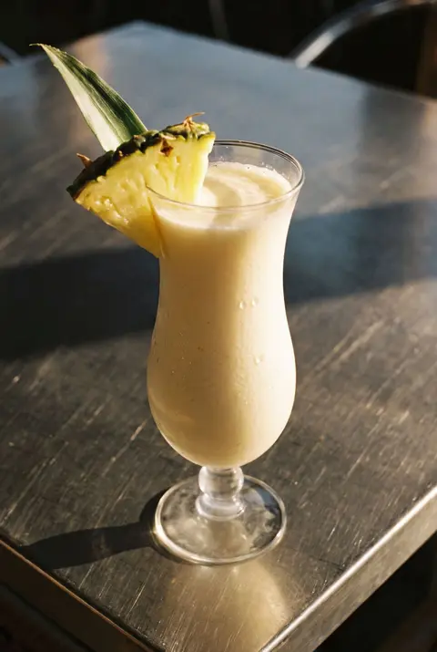 A creamy pina colada with a wedge of pineapple on the rim in a curved hurricane glass