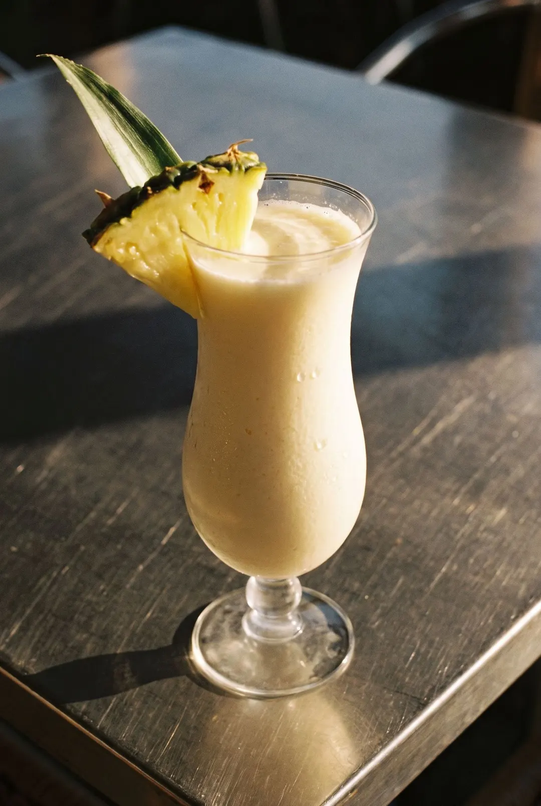 A creamy pina colada with a wedge of pineapple on the rim in a curved hurricane glass