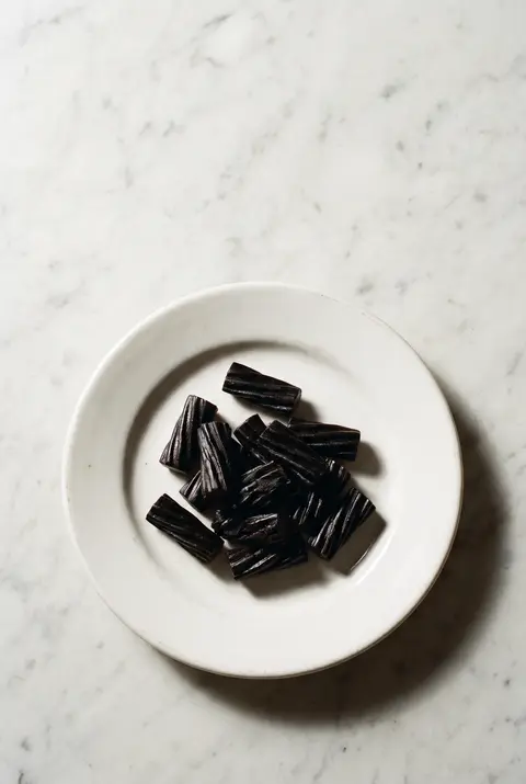 A small heap of black licorice pieces on a white plate