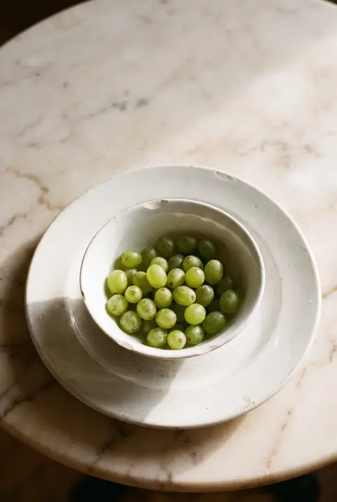A white porcelain bowl of green grapes on a white plate