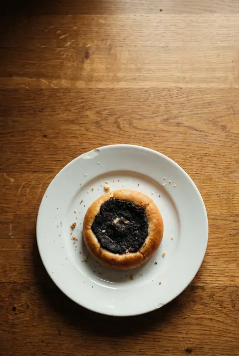 A round Czech kolac pastry with a poppy seed centre on a white plate
