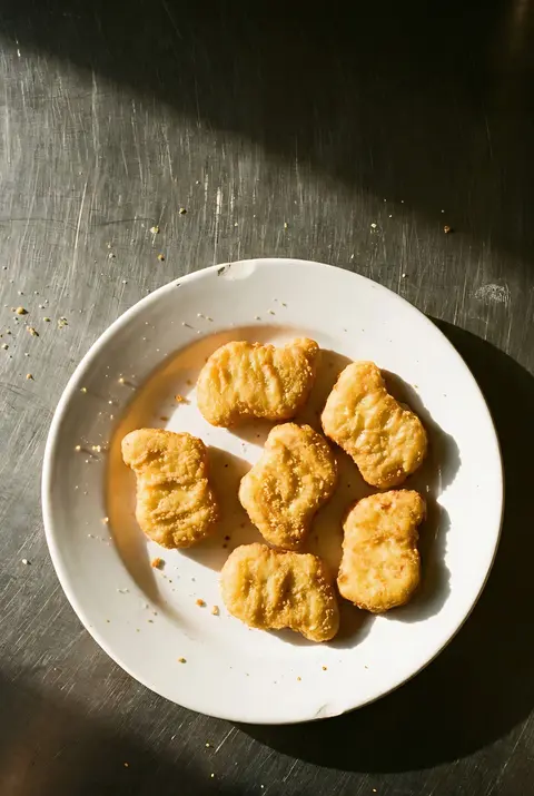 Six golden chicken nuggets on a white plate