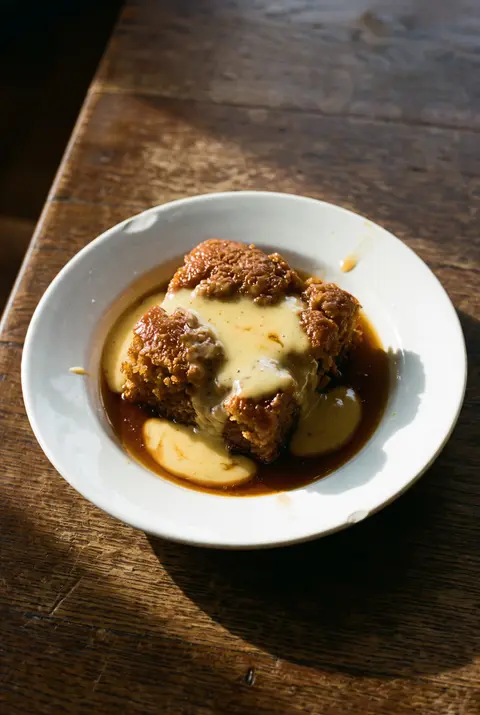 A portion of malva pudding with warm custard on a white plate