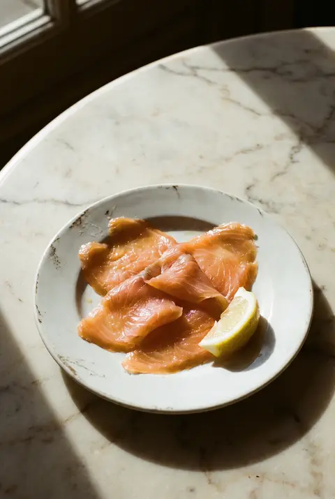 100 g of thinly sliced smoked salmon with a wedge of lemon on a white plate
