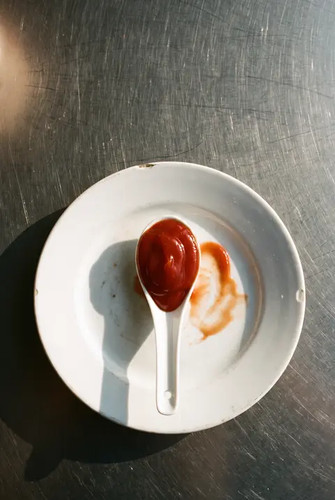 A tablespoon of tomato ketchup in a small white porcelain spoon on a white plate
